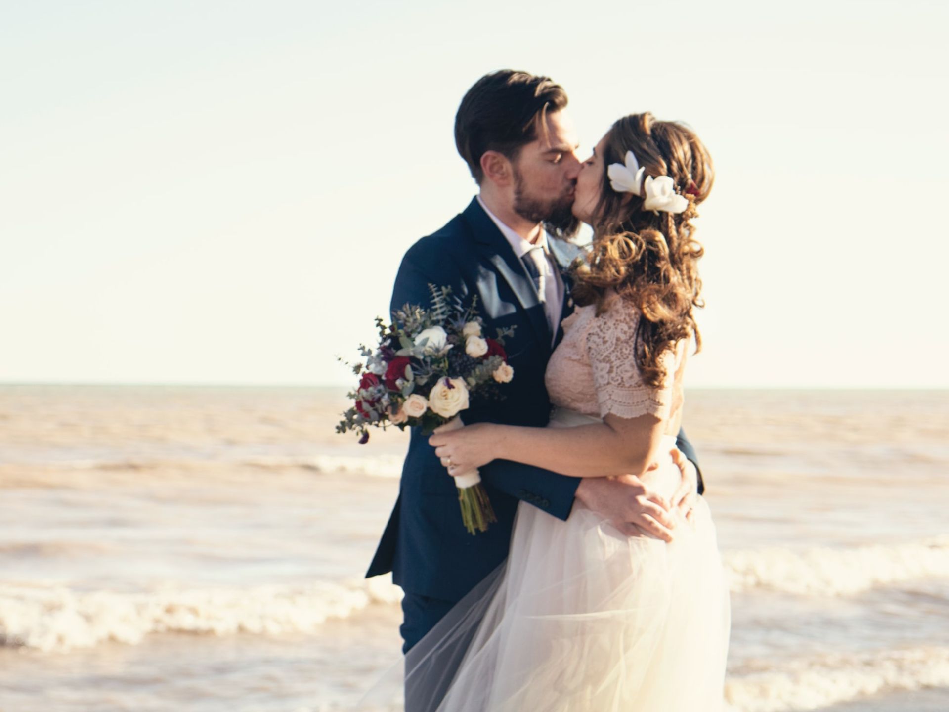A bride and groom kissing at the beach.