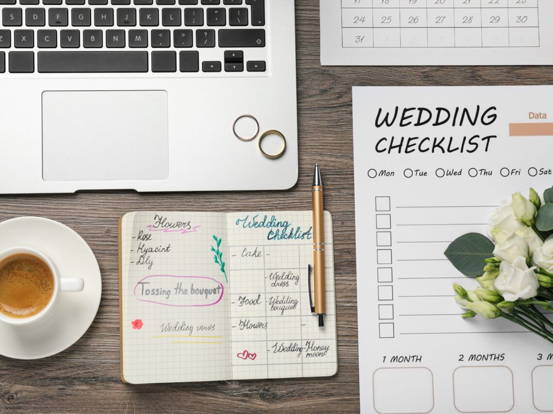 A wooden table with a wedding planning checklist and a grey laptop.