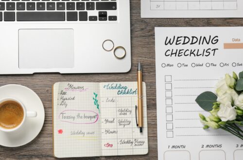 A wooden table with a wedding planning checklist and a grey laptop.