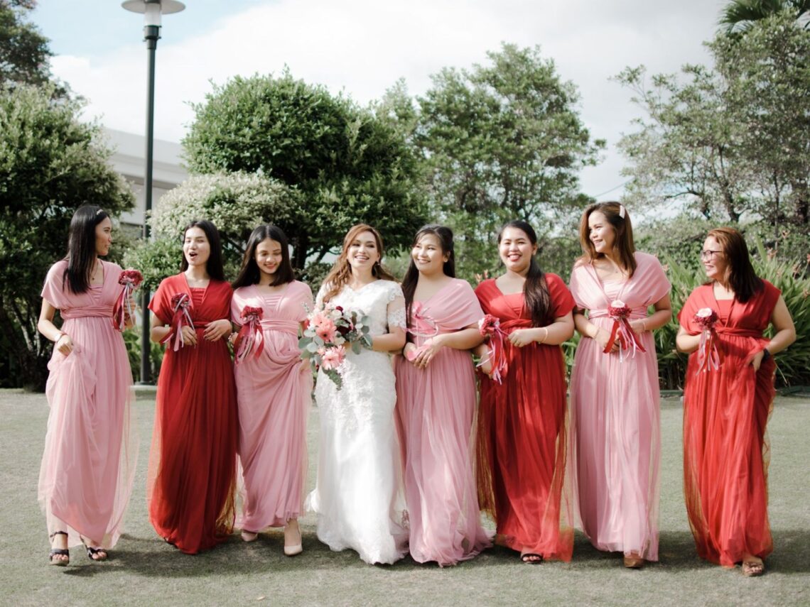 A group of bridesmaids wearing a mixture of red and light pink bridesmaid dresses.