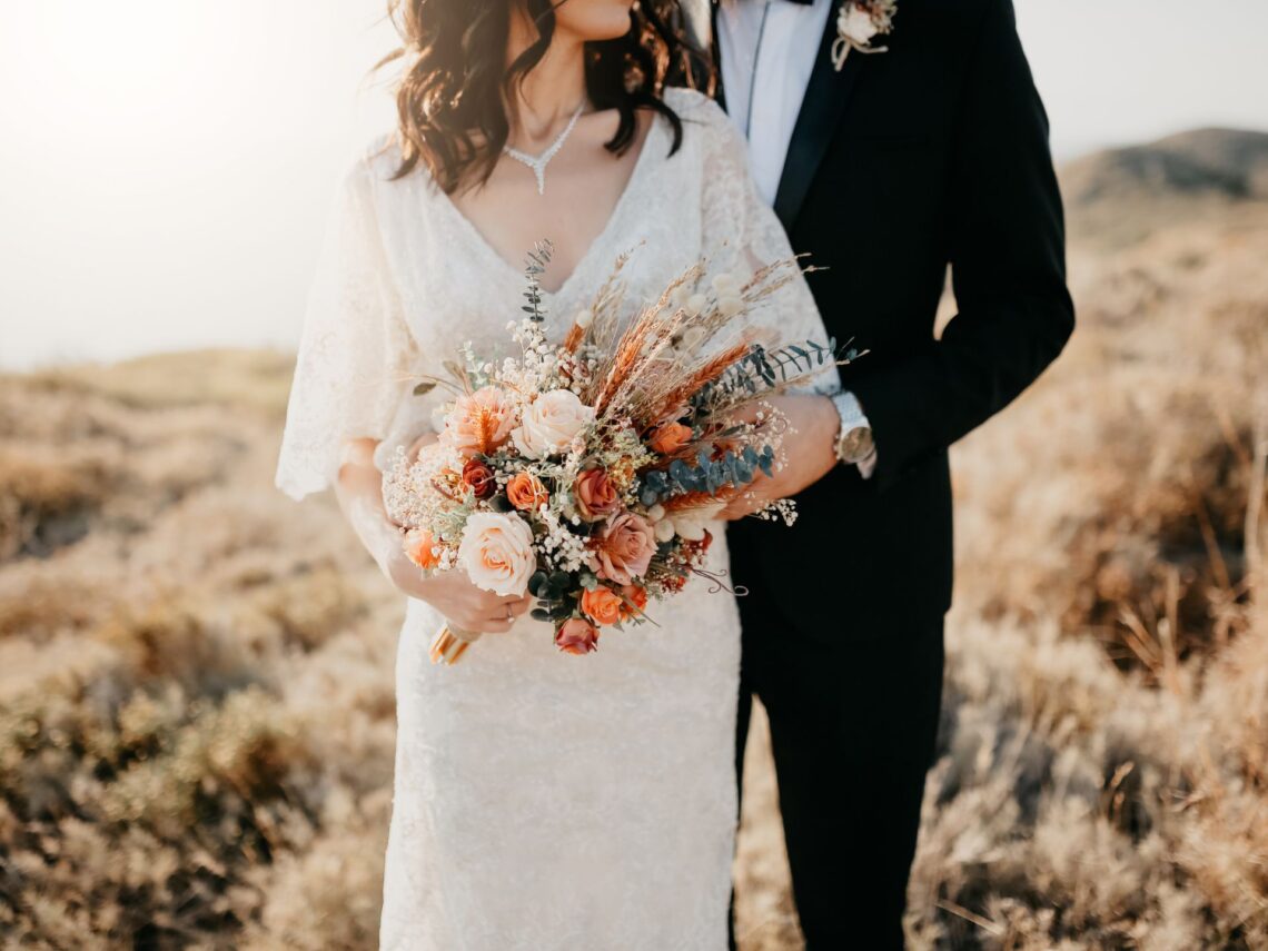 A bride holding rustic orange wedding bouquet.