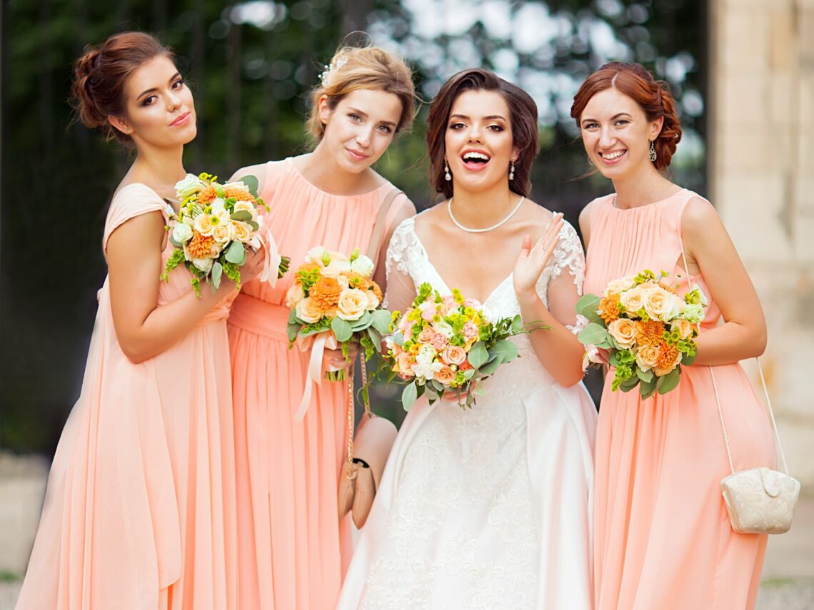 Bridesmaids wearing peach dresses and holding colorful flower bouquets.