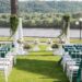 An outdoor wedding venue with white chairs that have emerald green sashes.