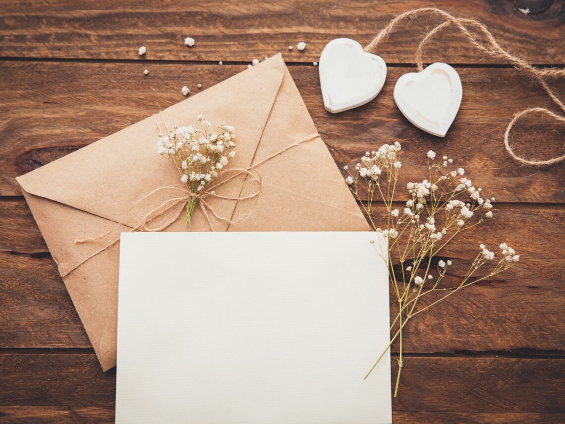 A wooden table with white rustic wedding invitations.