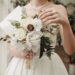 A bride holding a neutral colored wedding bouquet.