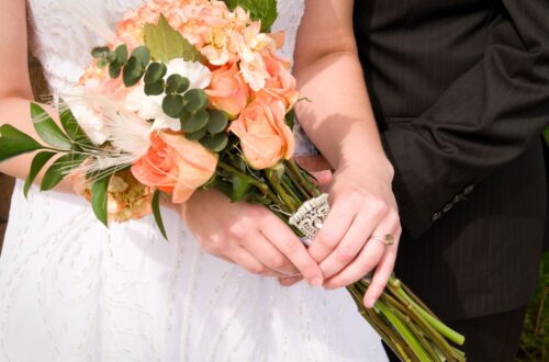 A bride carrying a peach colored wedding bouquet.