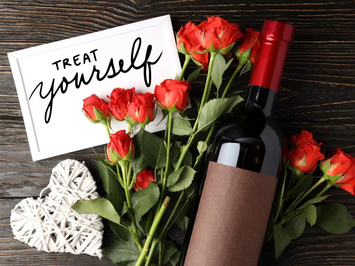 A wooden table with red wine and red roses on top.