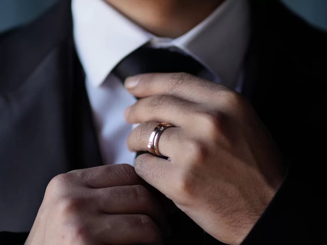 A groom putting on his tux and wedding ring.